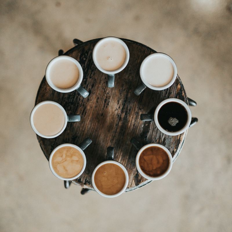 Eight cups of coffee arranged in a circle, from milky white to black